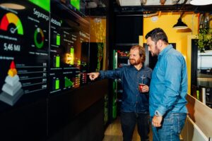 Dois profissionais analisam dados de telemetria veicular no painel da torre de controle da Addiante