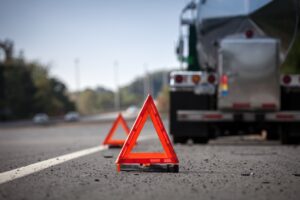 Triângulos de sinalização vermelhos posicionados na pista ao lado de um caminhão tanque parado no acostamento de uma rodovia durante o dia